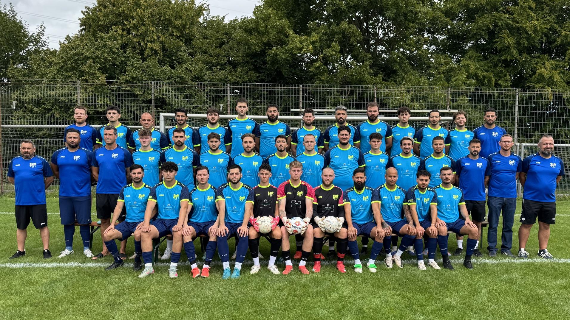 Mannschaftsbild von 60 Fu&szlig;ballspielern und Trainern in blauen Trikots auf einem Sportplatz mit Rasen.