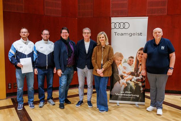 Sechsk&ouml;pfige Gruppe von Personen posiert vor einem Banner mit der Aufschrift &bdquo;Teamgeist&ldquo;.