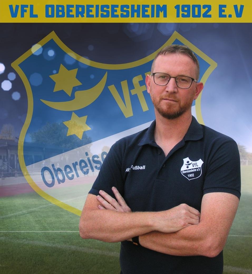 Portr&auml;t eines Mannes mit Brille, der in einem Fu&szlig;balltrikot steht. Im Hintergrund das Logo von VfL Obereisesheim.