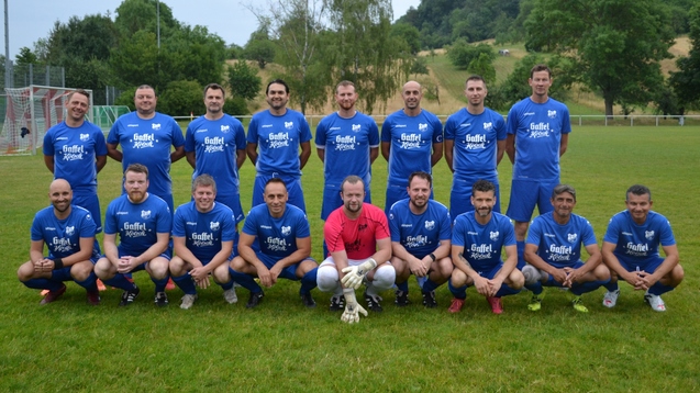 Mannschaftsfoto einer Fu&szlig;ballmannschaft in blauen Trikots auf einem gr&uuml;nen Platz, stehend und sitzend in zwei Reihen.