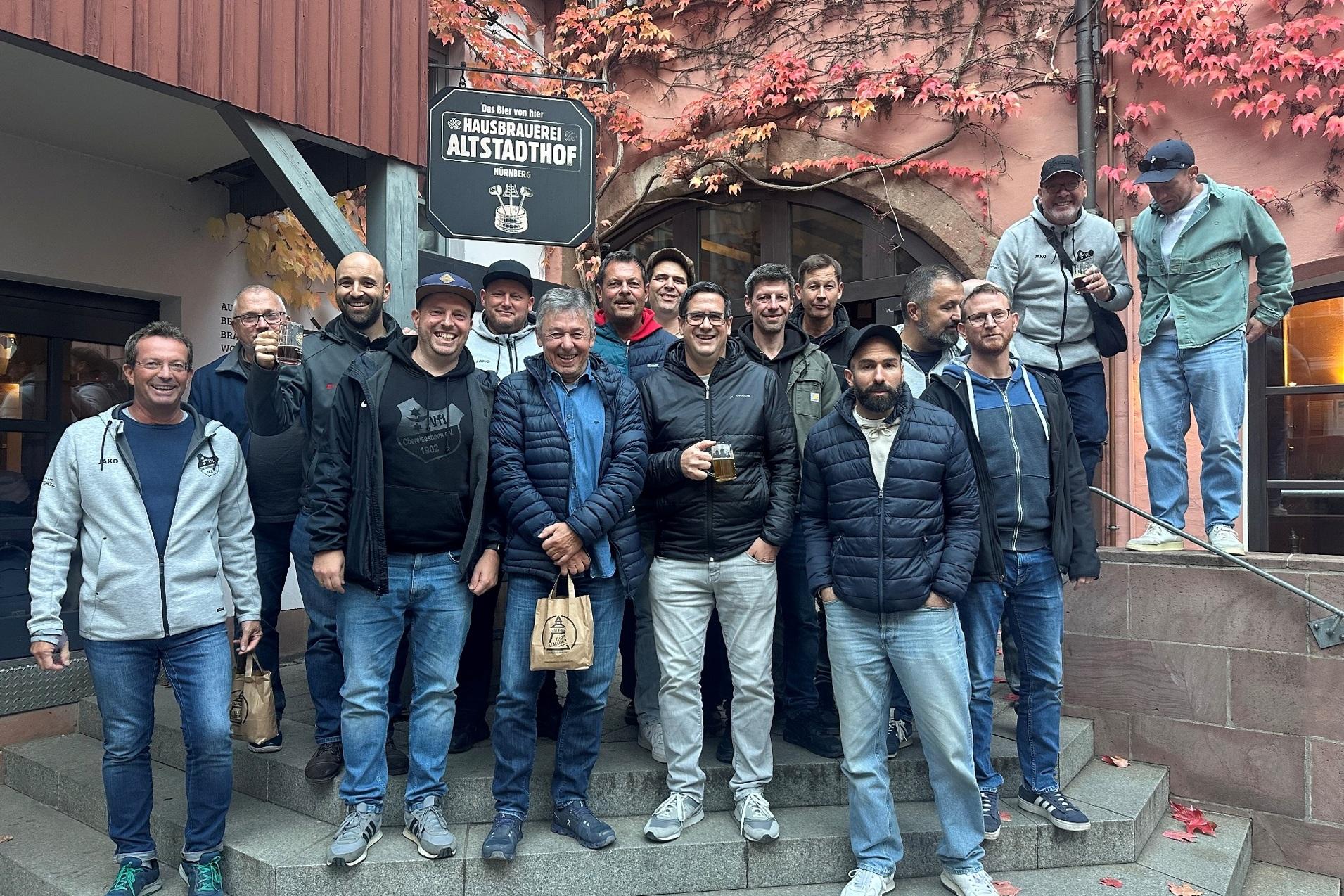 Gruppe von M&auml;nnern posiert auf Treppenstufen vor einem Restaurant mit herbstlicher Fassaden-Umgebung.