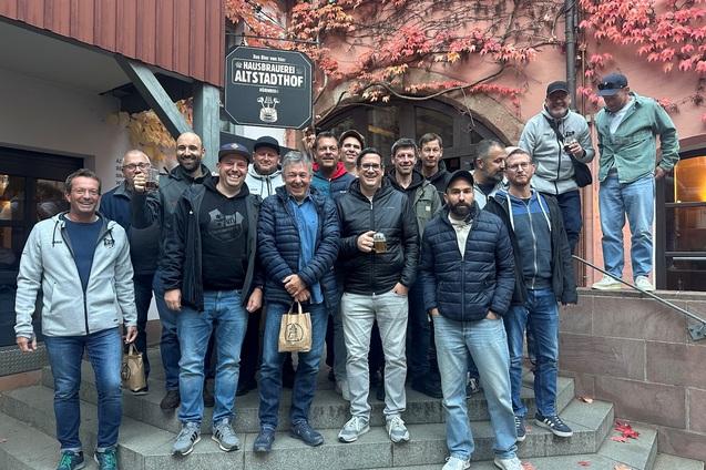 Gruppe von M&auml;nnern posiert auf Treppenstufen vor einem Restaurant mit herbstlicher Fassaden-Umgebung.