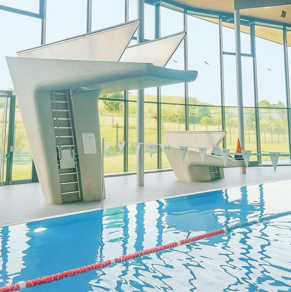 Sprungturm und Wettkampfschwimmbecken in einem modernen Hallenbad mit gro&szlig;en Fenstern und nat&uuml;rlichem Licht.