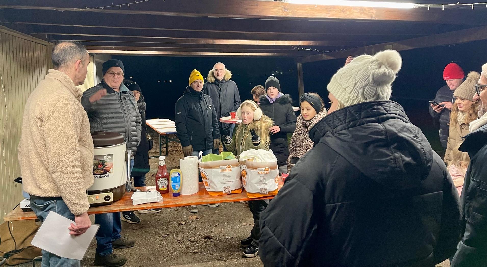 Gruppe von Menschen bei einem Abendessen im Freien, um einen Tisch mit Speisen und Getr&auml;nken versammelt.