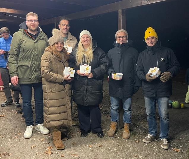 Gruppe von sieben Personen in Winterkleidung steht unter einem Vordach und h&auml;lt Boxen in den H&auml;nden.