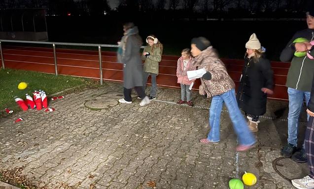 Kinder und Erwachsene spielen im Dunkeln auf einem Platz mit roten Bechern und bunten B&auml;llen.