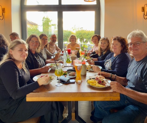 Eine Gruppe von zw&ouml;lf Menschen sitzt an einem gedeckten Tisch in einem Restaurant und genie&szlig;t verschiedene Speisen und Getr&auml;nke.