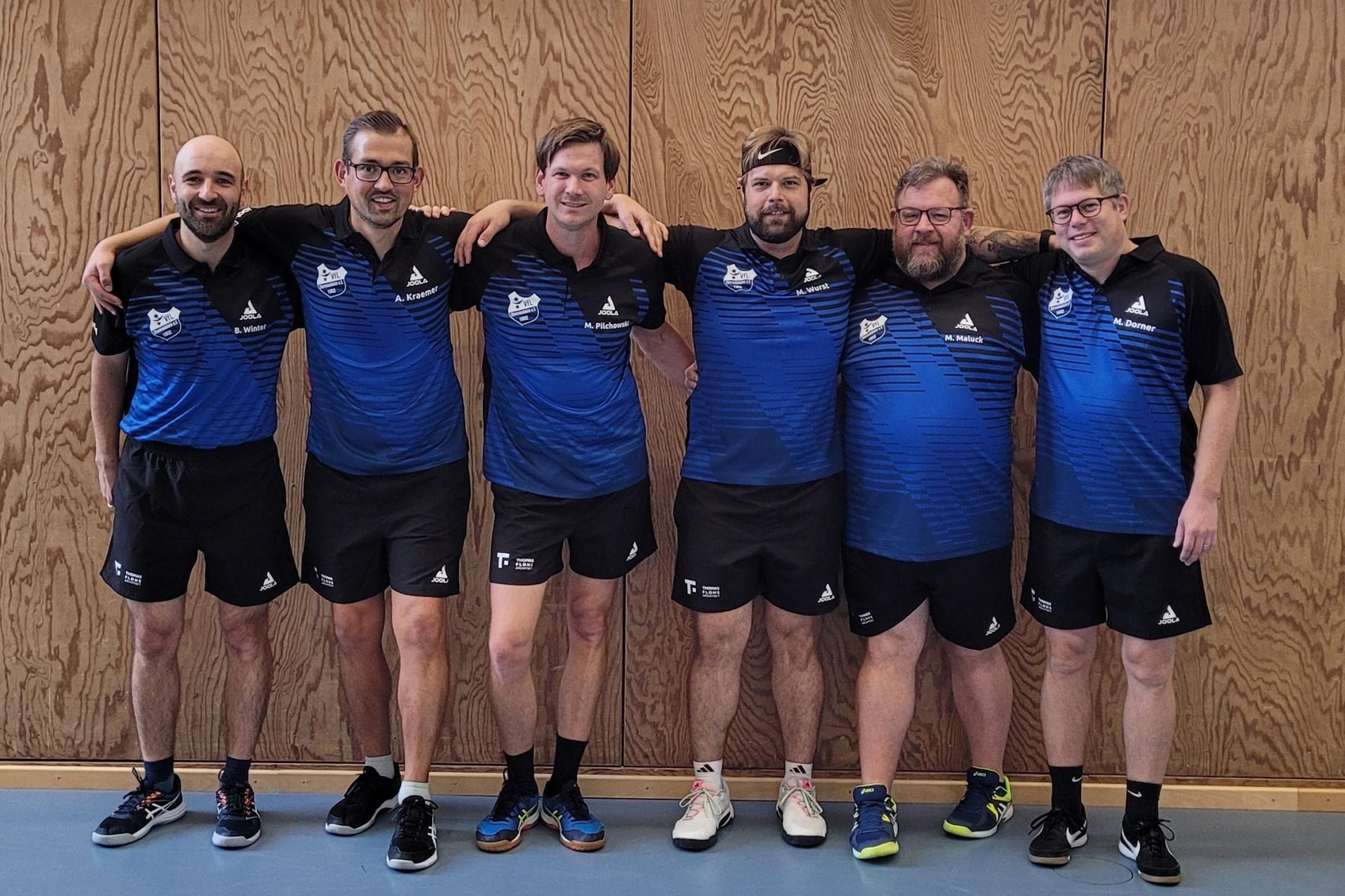 Sechs M&auml;nner in blauen Sportsch jerseys stehen gemeinsam l&auml;chelnd vor einer Holzwand.