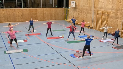 Gruppentraining in einer Halle: Erwachsene f&uuml;hren &Uuml;bungen auf Matten und mit Gewichten durch.