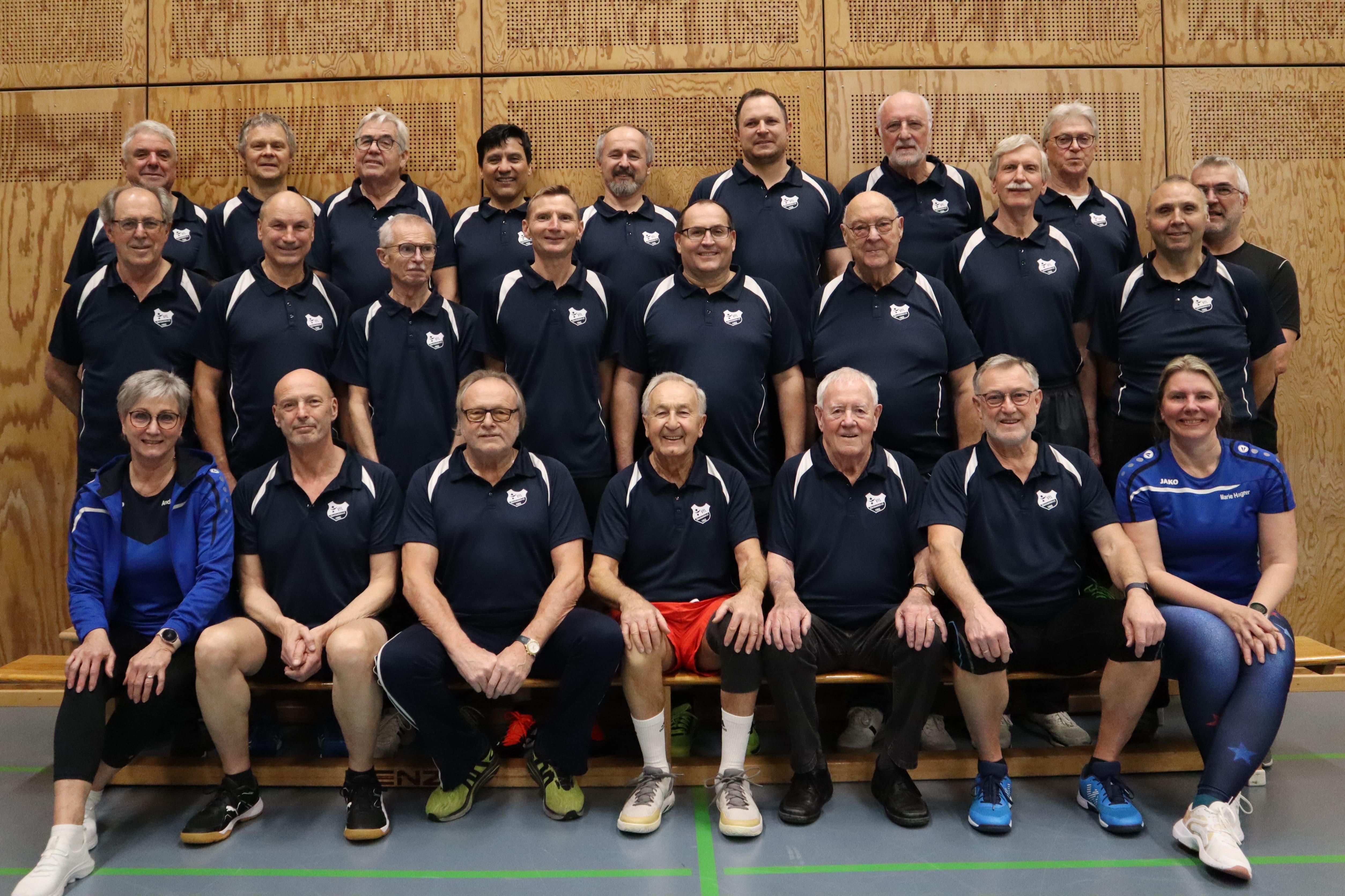 Gruppendarstellung von M&auml;nnern und einer Frau in sportlicher Kleidung, die auf einer Bank in einer Halle posieren.