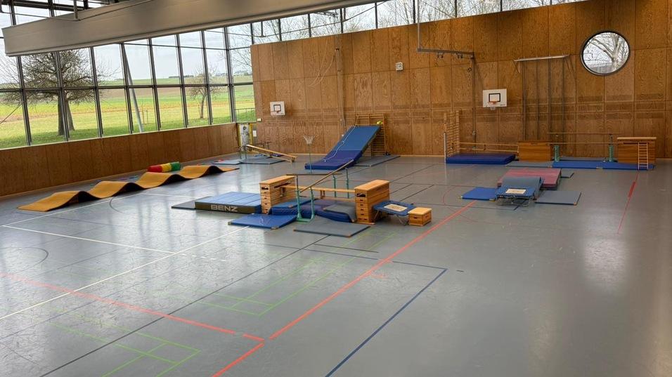 Gro&szlig;e Sporthalle mit Bewegungsger&auml;ten wie Matten, B&auml;nken und einer Rutsche, beschienen von Fensterlicht.