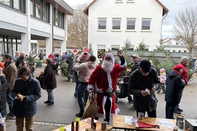 Weihnachtsmarkt mit Menschenmenge, darunter ein kost&uuml;mierter Weihnachtsmann, im Innenhof einer Schule.