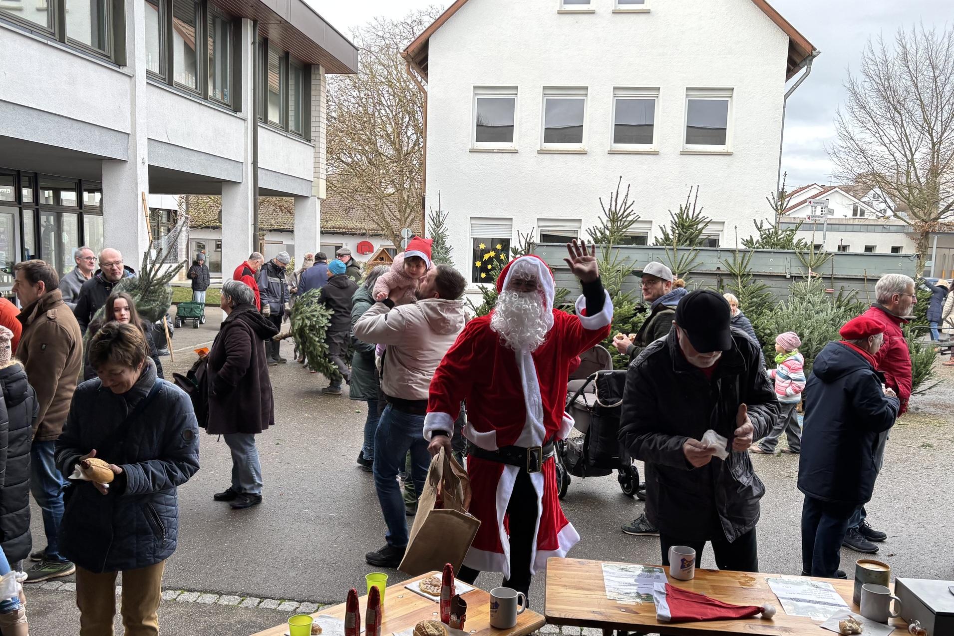 Weihnachtsmarkt mit Menschenmenge, darunter ein kost&uuml;mierter Weihnachtsmann, im Innenhof einer Schule.
